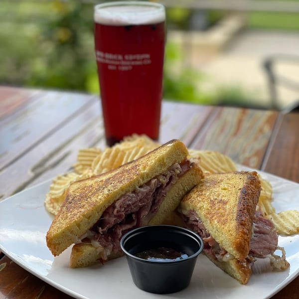 Red Brick Station's roast beef sandwich with chips and a pint of beer on a wooden table.