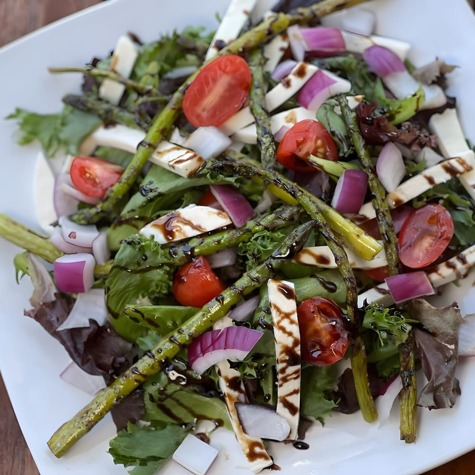A vibrant Red Brick Station salad with grilled asparagus, tomatoes, red onion, and mozzarella on greens.