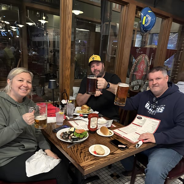 Three happy customers at Red Brick Station restaurant, toasting with beer mugs and enjoying their American food.