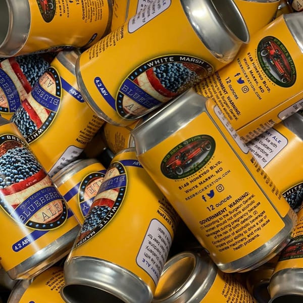 A close-up view of numerous Red Brick Station Blueberry Ale cans, featuring a patriotic label design.