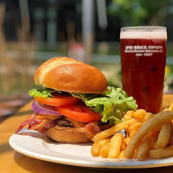 A Red Brick Station bacon cheeseburger with fries and a pint of beer on a white plate.