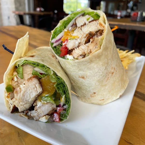 Two chicken wraps filled with lettuce, onions, peppers, and sauce, served with fries.