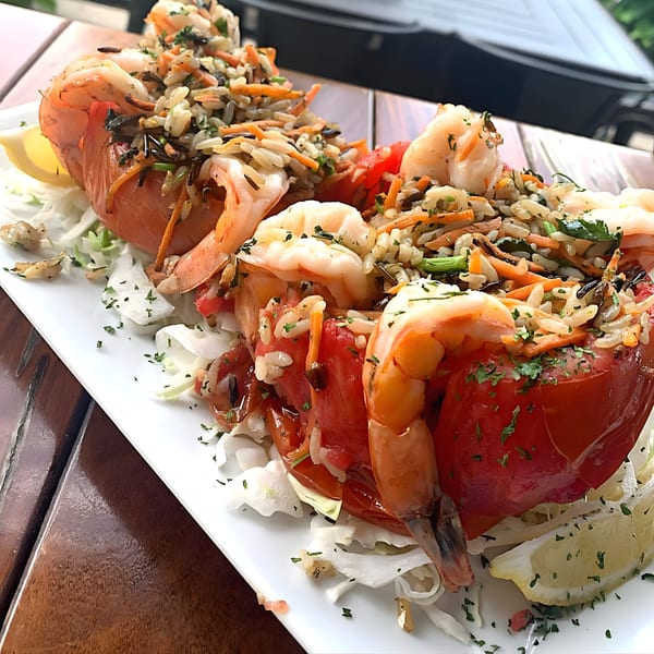 Shrimp and rice stuffed red bell peppers with lemon wedges on a white plate at Red Brick Station.