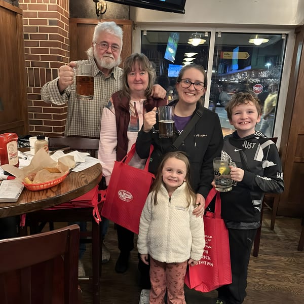 A family of five, including children, smiles while holding drinks and Red Brick Station bags.