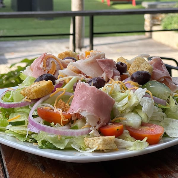 A large chef salad with ham, turkey, cheese, tomatoes, olives, and croutons on a white plate.