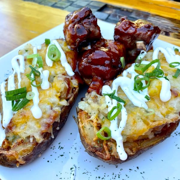 Two loaded potato skins with melted cheese, sour cream, and green onions, alongside BBQ ribs.